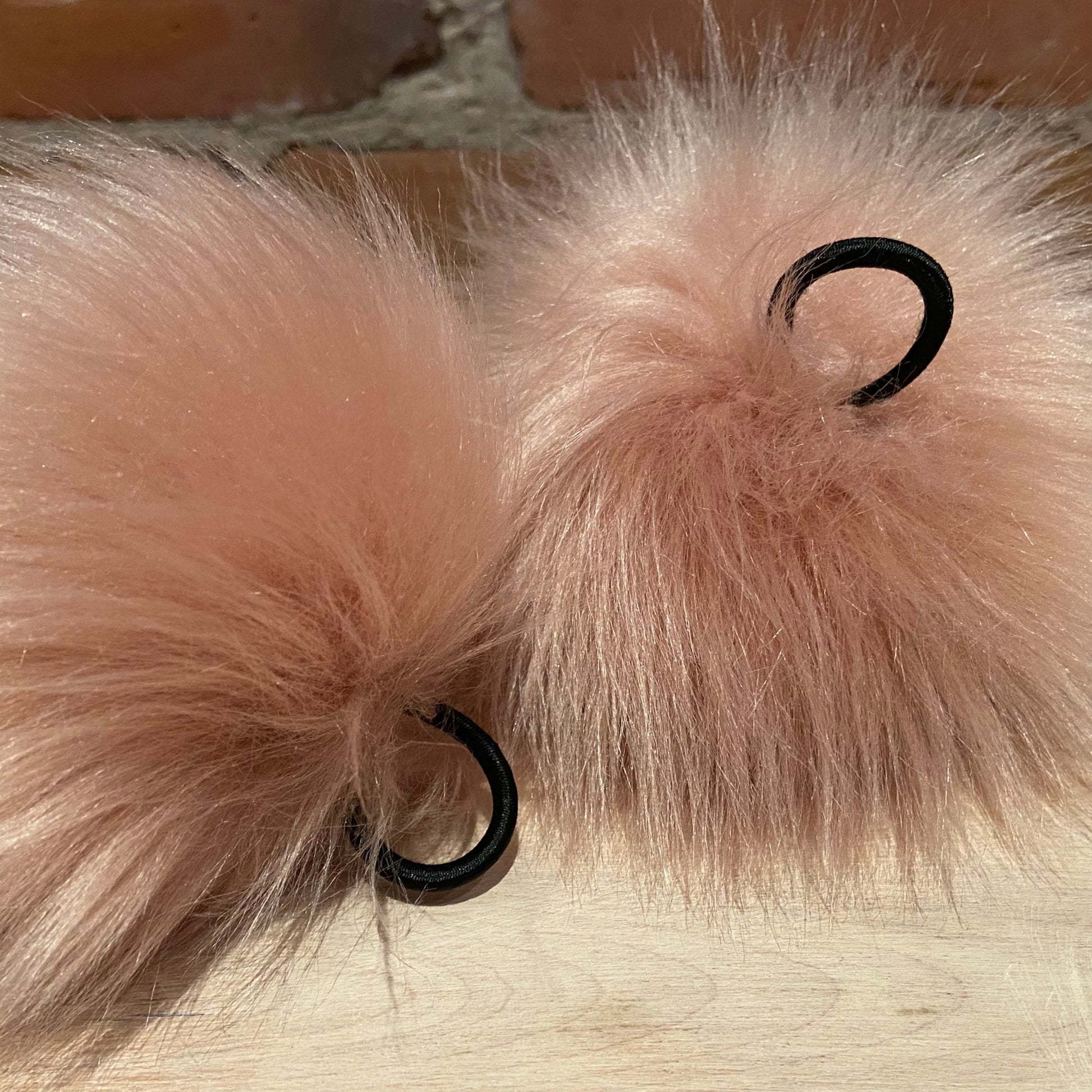 two pink faux fur poms upside down showing elastic loop attachments