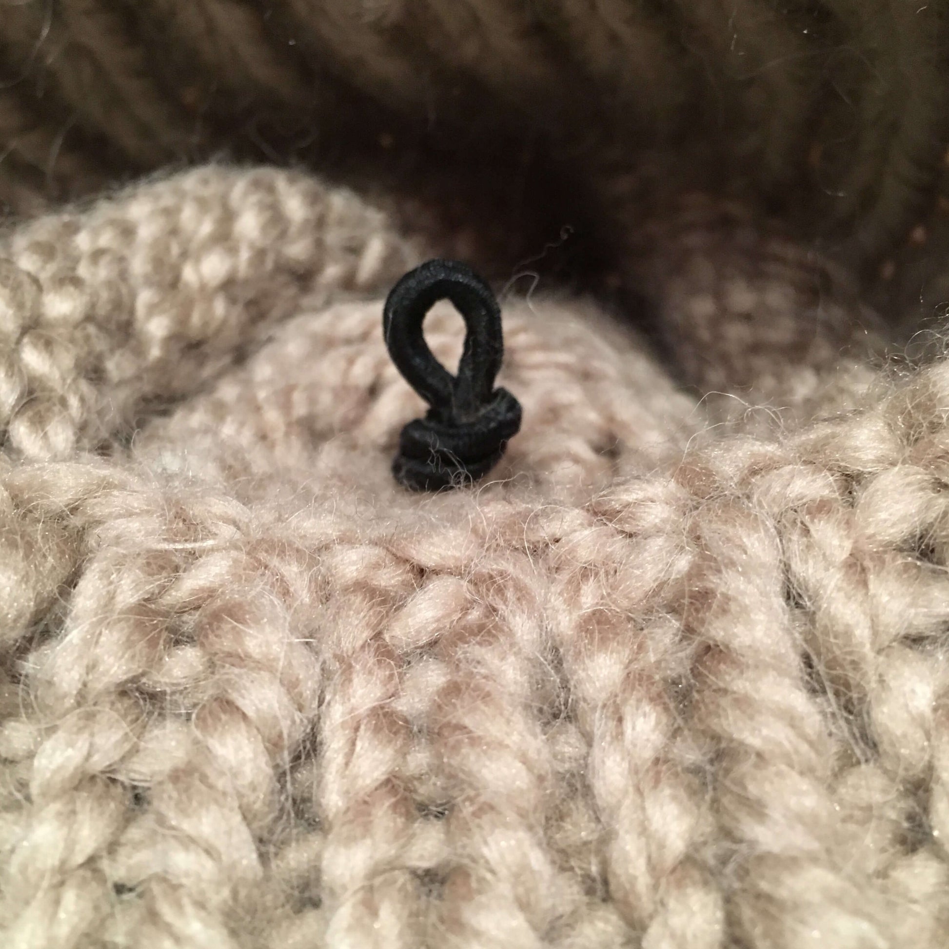 elastic loop attachment tied in knot inside beige knit hat, secured in place